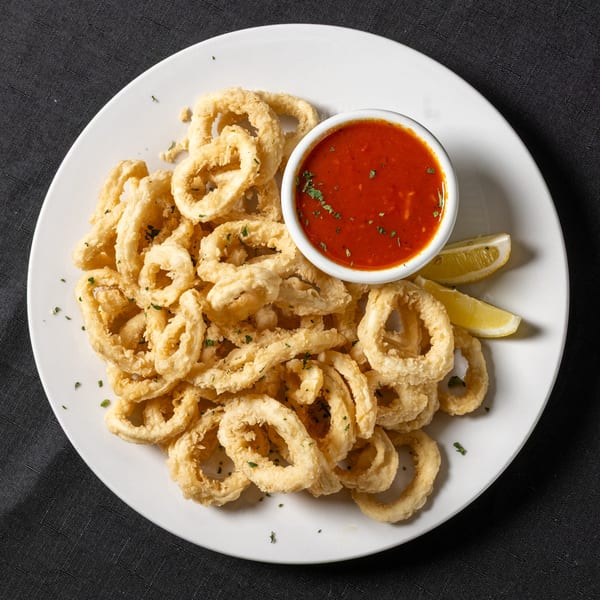 Crispy fried calamari rings with a side of red marinara sauce and lemon wedges.
