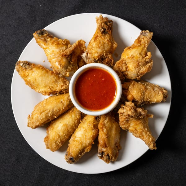 Crispy fried chicken wings arranged in a circle around a small bowl of red dipping sauce.