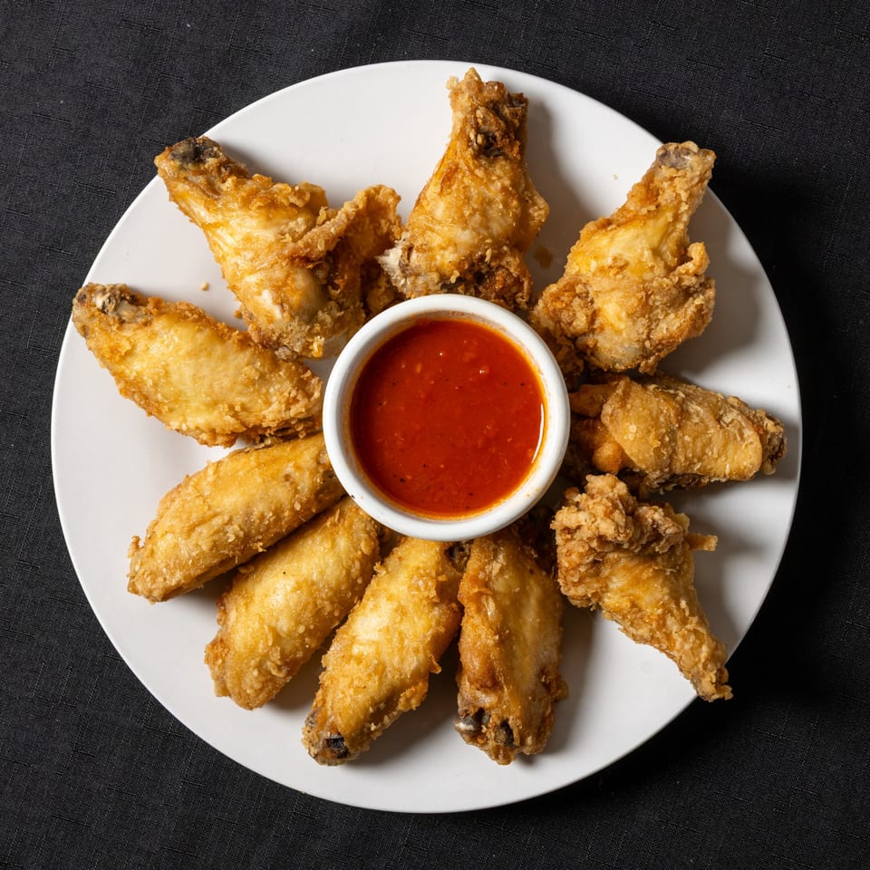 Crispy fried chicken wings arranged in a circle around a small bowl of red dipping sauce.
