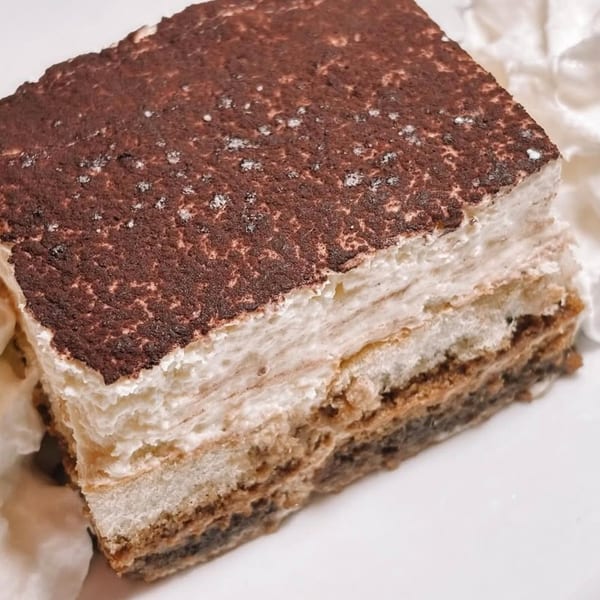 A close-up of a tiramisu slice with layers of cream and cake, topped with cocoa powder.