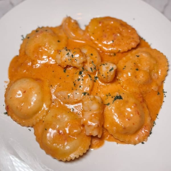Shrimp ravioli in a creamy orange sauce, garnished with herbs on a white plate.