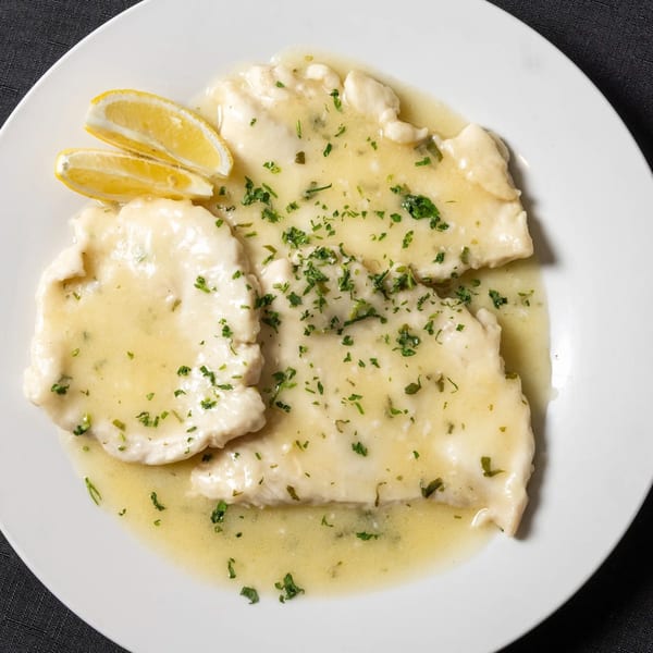 Chicken Francese with lemon wedges and parsley on a white plate from Vinnie's Pizzeria.