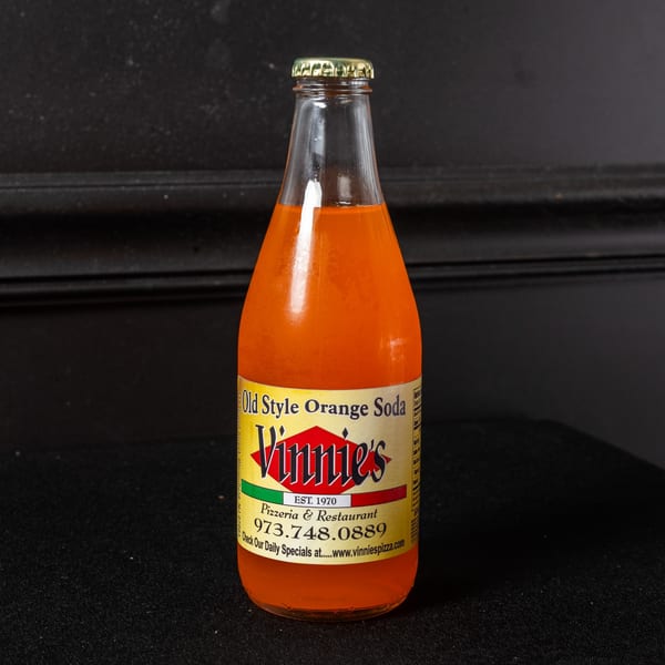 A glass bottle of Vinnie's Old Style Orange Soda with a yellow label against a dark background.