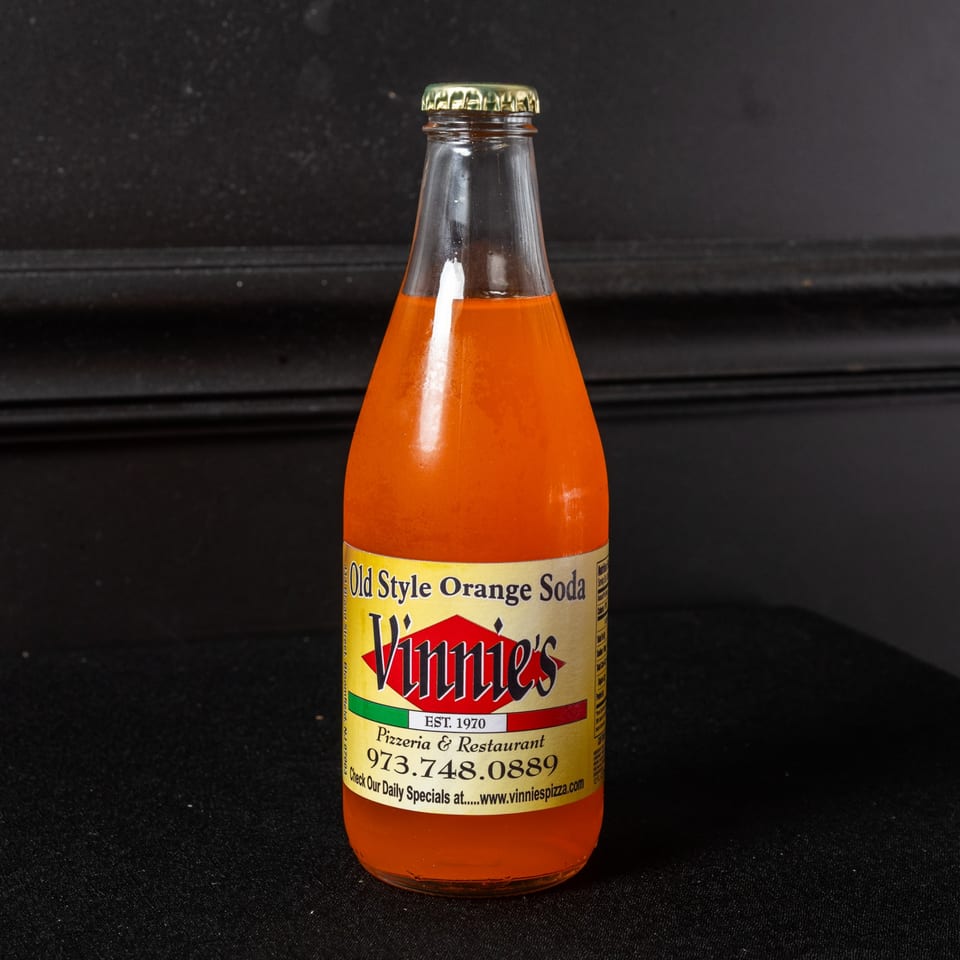A glass bottle of Vinnie's Old Style Orange Soda with a yellow label against a dark background.