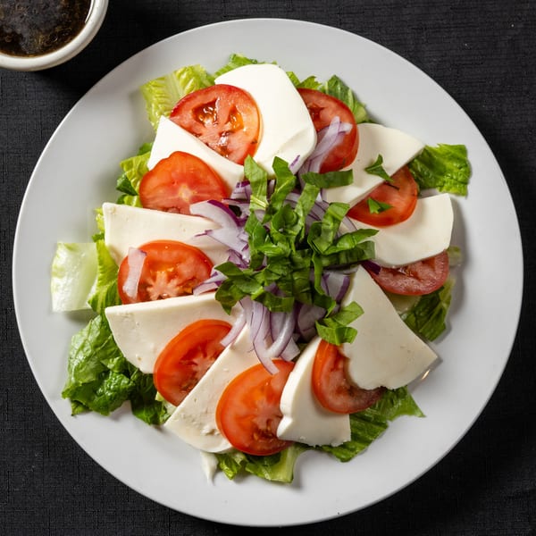 Caprese salad with fresh mozzarella, sliced tomatoes, red onion, and basil on lettuce.