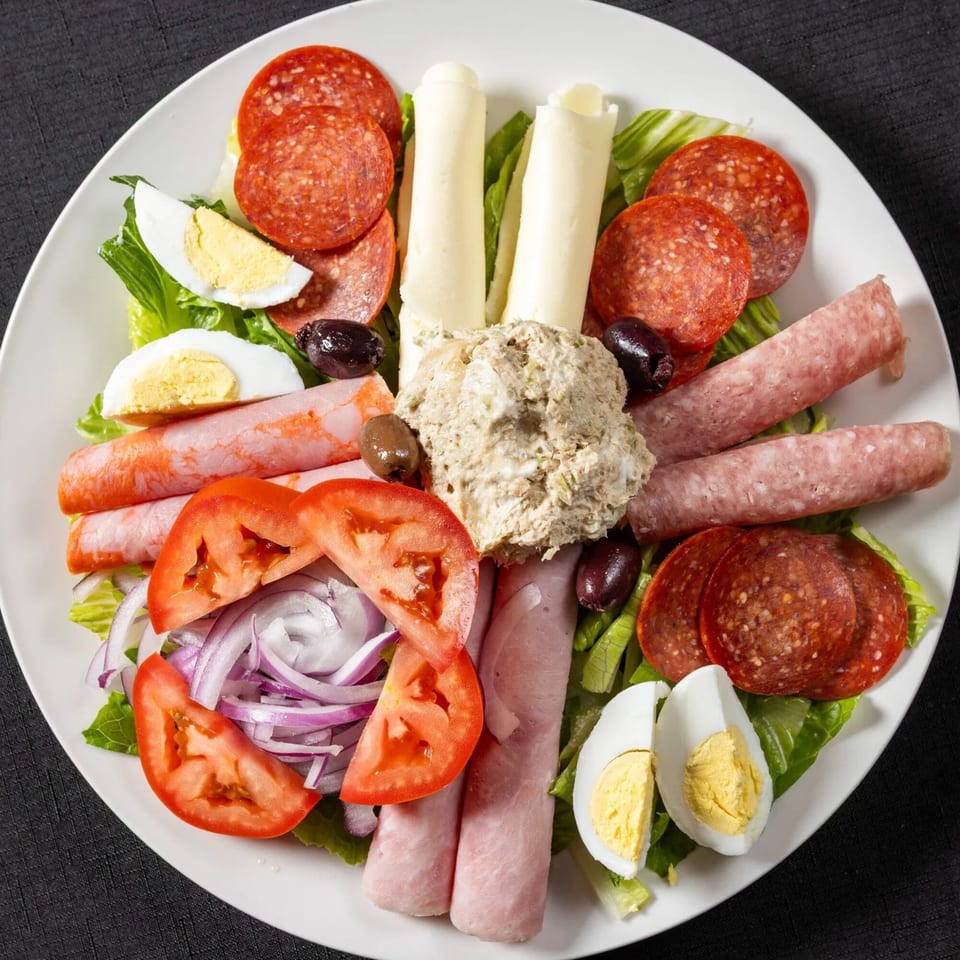 Antipasto salad with pepperoni, ham, salami, provolone, tuna, tomatoes, onions, olives, and hard-boiled eggs.