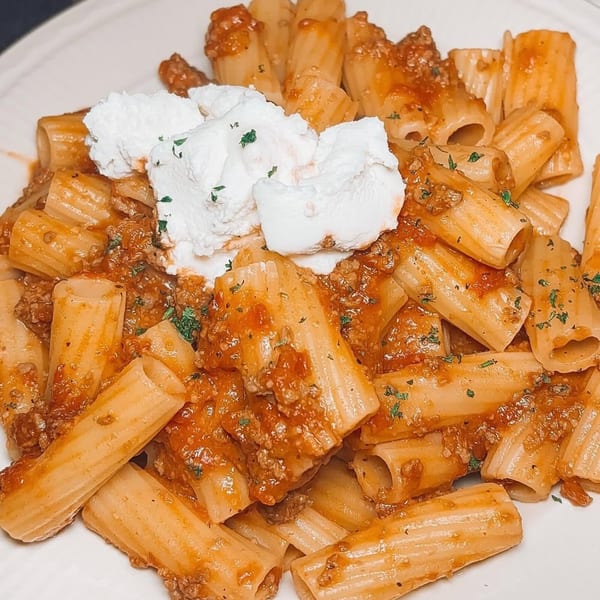 Rigatoni pasta with meat sauce and a dollop of ricotta cheese, garnished with parsley.
