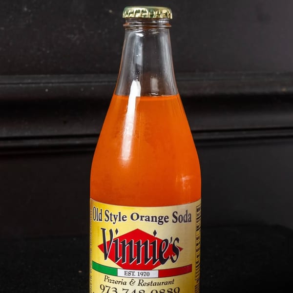 A bottle of Vinnie's Old Style Orange Soda with a gold cap against a dark background.