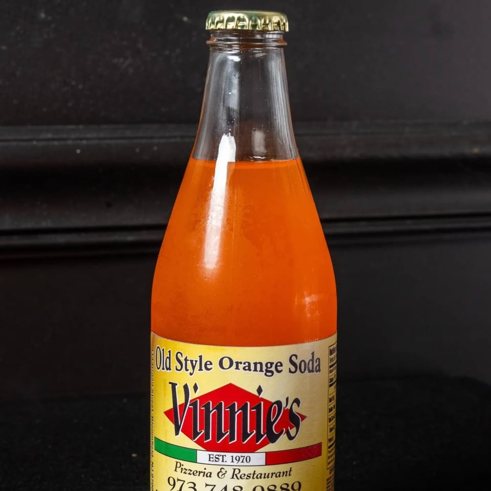 A bottle of Vinnie's Old Style Orange Soda with a gold cap against a dark background.