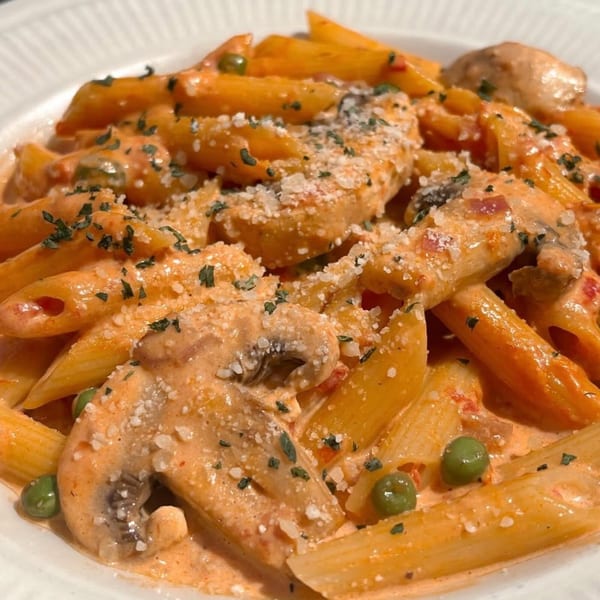 Penne pasta with creamy pink sauce, mushrooms, peas, and parsley, topped with grated cheese.