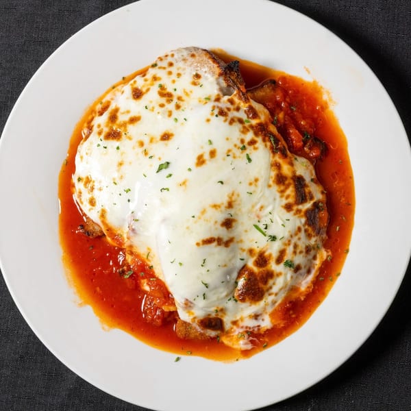 Chicken Parmesan with melted mozzarella cheese and red sauce on a white plate from Vinnie's Pizzeria.