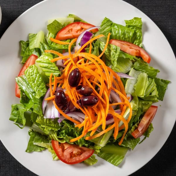 Fresh garden salad with lettuce, tomatoes, red onion, shredded carrots, and olives on a white plate.