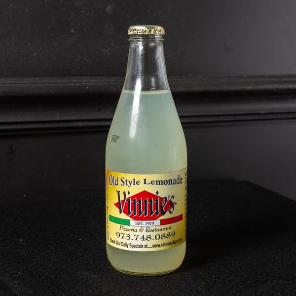 A glass bottle of Vinnie's Old Style Lemonade with a gold cap on a dark background.