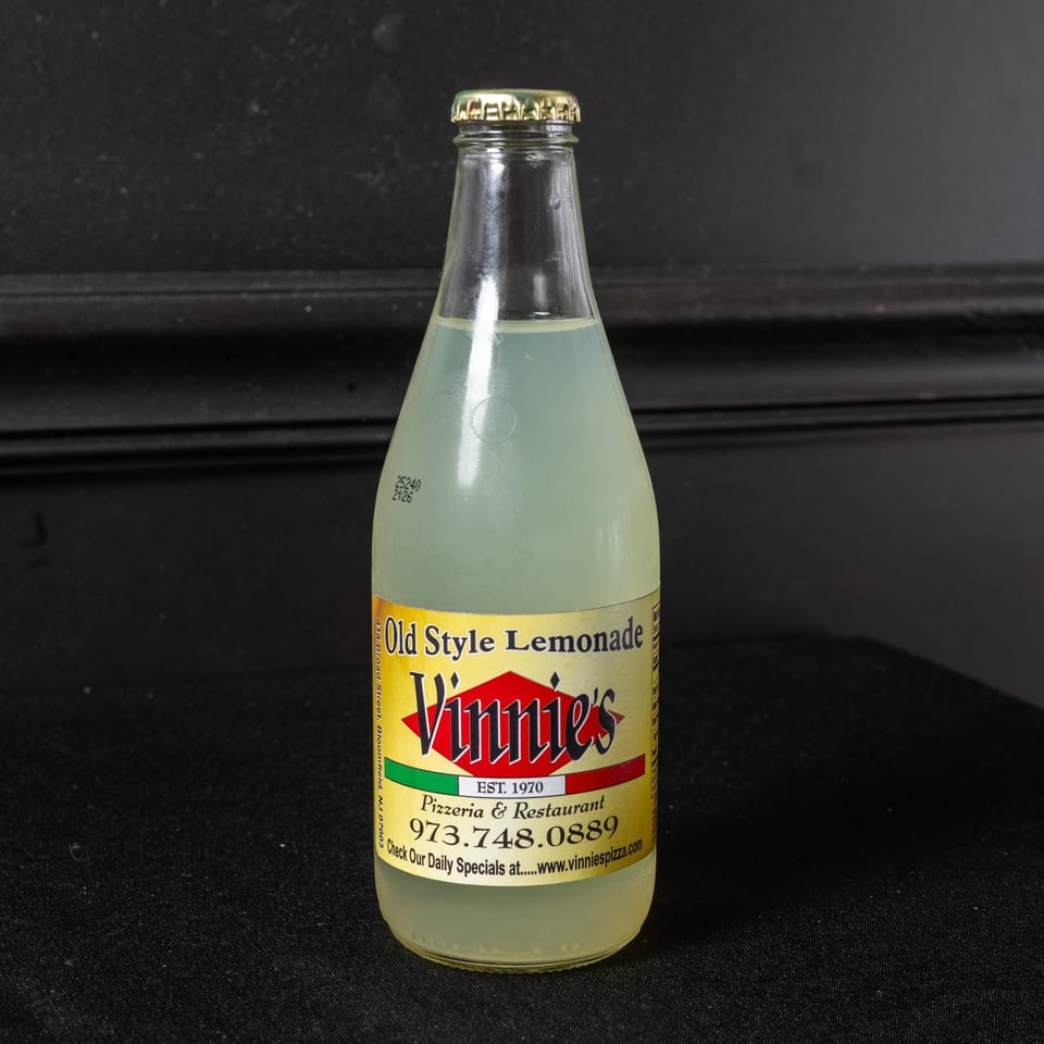 A glass bottle of Vinnie's Old Style Lemonade with a gold cap on a dark background.