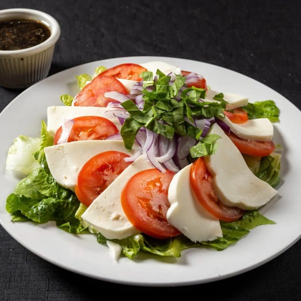 Fresh Caprese salad with mozzarella, tomatoes, red onion, and basil, with a side of dressing.