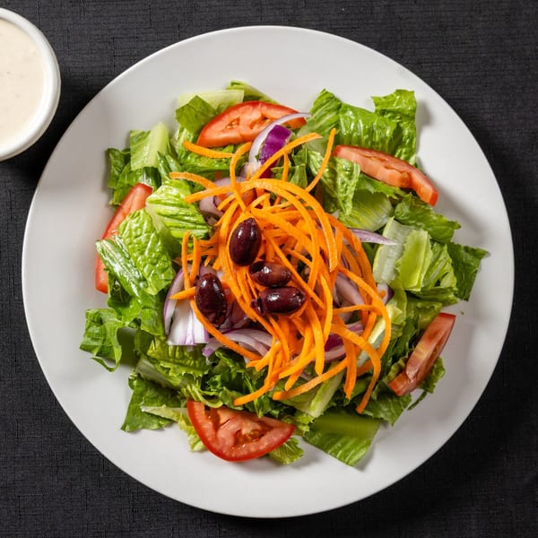 Fresh garden salad with lettuce, tomatoes, red onions, shredded carrots, and olives, with dressing on the side.