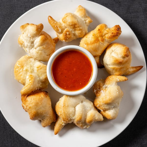Vinnie's Pizzeria garlic knots, sprinkled with salt, arranged around a small bowl of red marinara sauce.