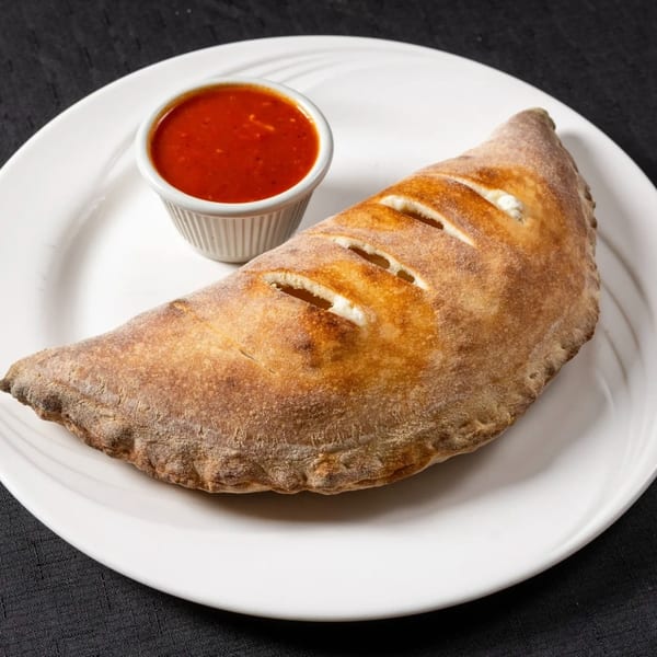 A golden-brown calzone with visible cheese filling and a side of red marinara sauce on a white plate.