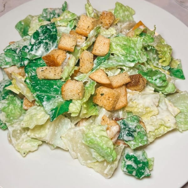 A close-up of a Caesar salad with crisp lettuce, creamy dressing, and golden croutons on a white plate.